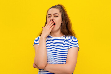 Young attractive woman wearing in white-blue striped t shirt feeling tired after night without sleep, yawning, covering opened mouth with palm. Restless and sleepiness
