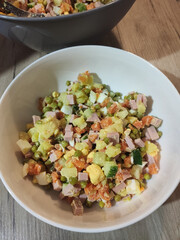 olivier salad in a white bowl in the kitchen