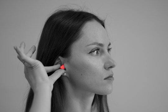 The woman takes earplugs out of her ears. Black and white photo with a bright accent on the earplug.
