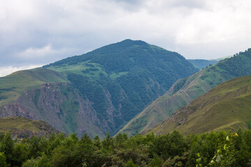Obraz premium Dramatic landscape - steep cliffs and green hills with cloudy sky and fog on a summer day in the Elbrus region North Caucasus russia and soft blurred focus