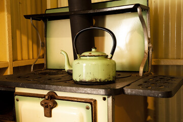Green enamel water kettle on an old fashioned wood stove.