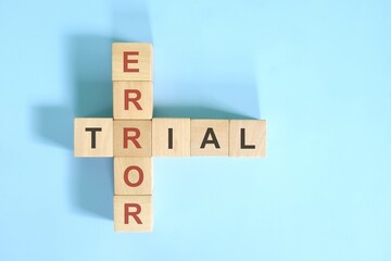 Trial and error approach concept. Wooden block crossword puzzle flat lay in blue background.