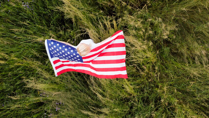 full length blond Woman holding American Flag in trees shadow of sunlight Back view cute blondy girl run on fresh green grass texture