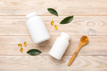 Omega-3 capsules lie in white bottle on a table with green leaves background. Fish oil tablets....