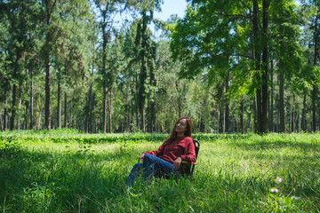 Naklejka na ściany i meble Portrait image of a beautiful young asian woman with closed eyes sitting on a chair in the park