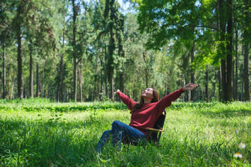 Portrait image of a beautiful young woman stretching arms while sitting and relaxing on a chair in the park