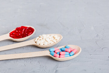 Vitamin capsules in a spoon on a colored background. Pills served as a healthy meal. Red soft gel vitamin supplement capsules on spoon