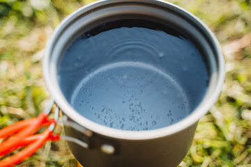 Tourist utensils for cooking in nature, a pot of water boils on the burner, air bubbles rise to the surface of the water, warm the tea.