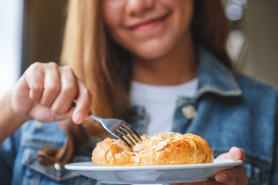 Closeup image of a young woman holding and eating a fresh almond croissant