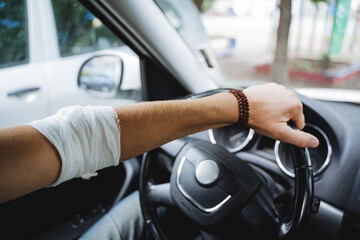 The guy sits behind the wheel of the car, the injured hand lies on the steering wheel, the elbow hurts, the joint is bandaged, the man's hand is in the car.