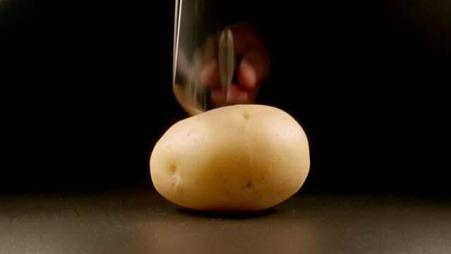 SLOW: Big knife cuts a row potato on a black background
