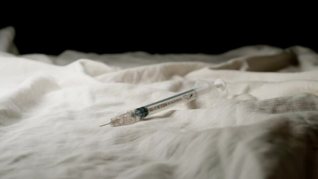 SLOW MOTION: Syringe falls on a bed