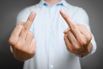 Naklejka premium Aggression, negativity, angry symbol concept. Close-up of caucasian man in shirt showing an obscene gesture with two hands, sign of middle finger of hand on gray background.