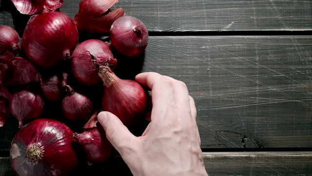 TOP VIEW: Human hand puts a red onion bulb on a black table