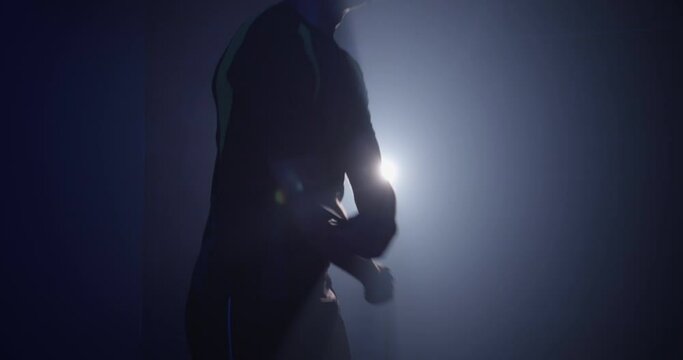 A young man exercising with a skipping rope, training in a dark room