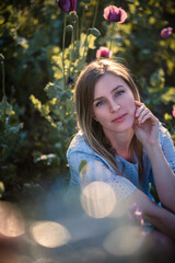 Woman with beautiful blue eyes is posing in poppy field wearing cute blue dress during summer sunset