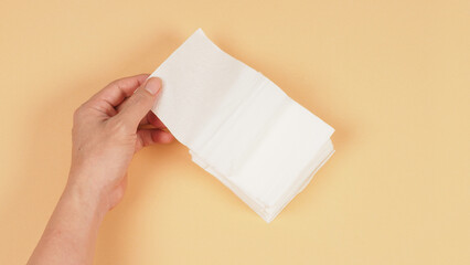 The hand is holding a small size of white paper tissues on a creamy ivory color background.