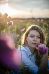 Romantic summer portrait of beautiful blonde woman in the middle of purple poppy field.
