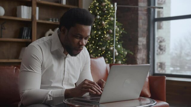Young adult african american guy recieving good news on his laptop with a win dance on Christmas
