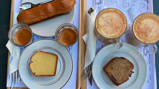 Paris, France. A rich breakfast with typical sweets and cappuccino and coffee. The hand grabs a biscuit and then the cup of coffee. View from above.