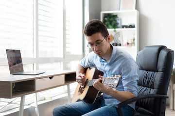 Young caucasian man practicing guitar at home