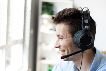 Close up photo of handsome man 20s wearing office clothes and headset working on computer in call center.