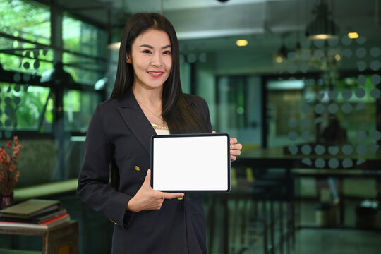 Confident millennial woman in business suit holding digital tablet, empty screen for your advertise text
