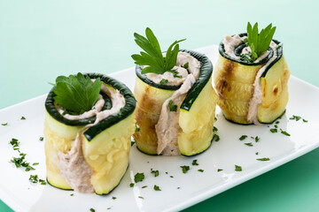 Grilled zucchini rolls with tuna and cream cheese on green background