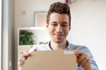 Close up of happy amazed young man consumer holding opening cardboard box sit on sofa at home, order postal shipping courier delivery concept.