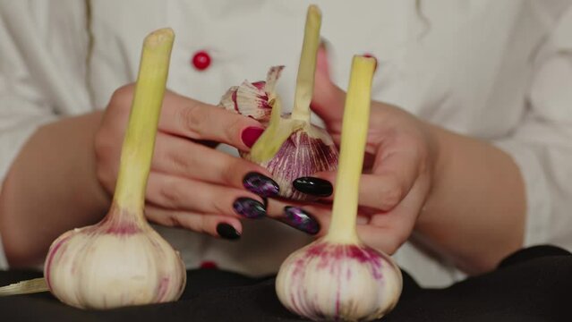 Close-up, an unrecognizable girl cook is peeling young garlic. Woman peels fresh garlic from the skin on the kitchen table