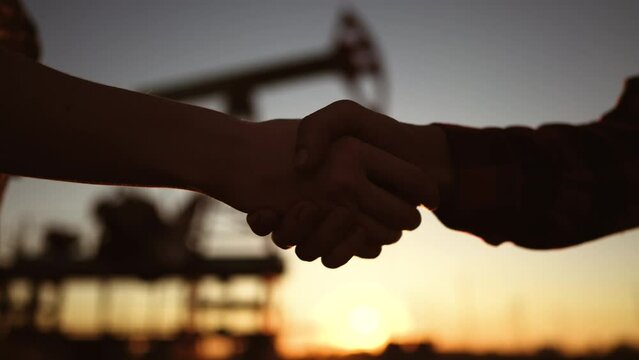handshake oil contract. handshake a worker and businessman shaking hands against the backdrop of an oil pump. oil extraction close-up business concept. silhouette handshake business contract