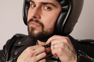 Cropped portrait of bearded biker in leather jacket fasten a motorcycle helmet.