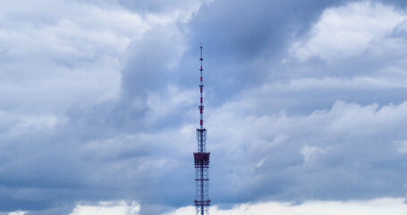 Obraz premium Telecom antenna tower on gray clouds background. TV spit aims at cloudy sky in overcast day. Telecommunication technology broadcasts television signal