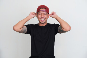 Tattooed asian man smiling excited while putting backward cap in his head