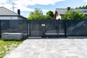 A modern panel fence in anthracite color, a visible sliding gate to the garage and a wicket with a letterbox. - obrazy, fototapety, plakaty