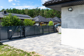 A modern panel fence in anthracite color, a visible sliding gate to the garage and a wicket with a...