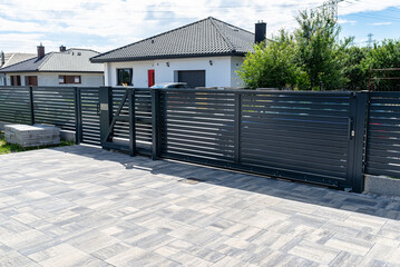 A modern panel fence in anthracite color, a visible sliding gate to the garage and a wicket with a...