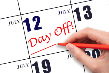 Hand writing text DAY OFF and drawing a line on calendar date 12 July. Vacation planning concept.