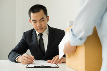 Desperately fired female office worker employee hands her employer her resignation letter and packs her belongings in a cardboard box concept dismissal and unemployment