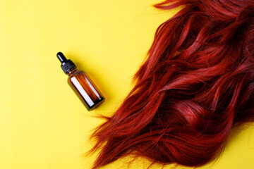 Hair care product in dropper bottle and red hair on yellow background. Mockup with unlabeled beauty...