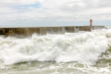 Waves crashing against the harbour wall in Porto, Portugal, Europe.  Lighthouse in view, space for text, showing strength, natural power and ferocity of the sea 17 MAY 2022