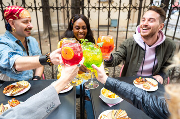 Multi ethnic friends toasting with coloured cocktails drinks at bar in the city centre - Group of...