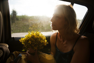 middle aged woman with a bouquet of yellow fragrant medicinal field herbs driving in a car from...