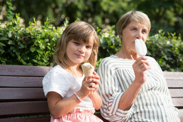grandmother and child granddaughter eat ice cream in the park on a summer day. happy family has fun together in nature