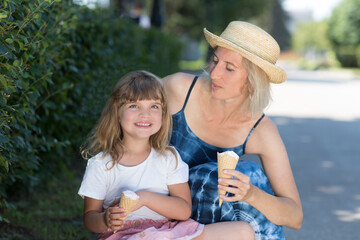 Mom and child daughter eat ice cream in the park on a summer day. happy family has fun together in nature