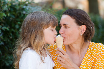 Mom and child daughter eat ice cream in the park on a summer day. happy family has fun together in nature