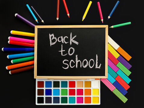 black chalk board with handwritten Back to school with school felt-tip pens, paints, pen, plasticine, on black background top view