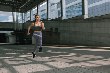 Fototapeta na wymiar Beautiful young woman in sportswear running strides outdoors on sunny summer day.