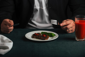 man at dinner consisting of delicious grilled beef steak and bright red tomato juice poured into a glass
