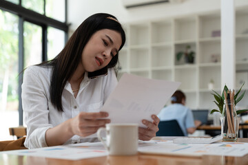 Business asian woman working with paperwork calculator at office while talking on phone,